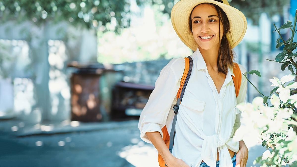 portrait happy carefree woman tourist in straw hat, white shirt walking and exploring small streets.