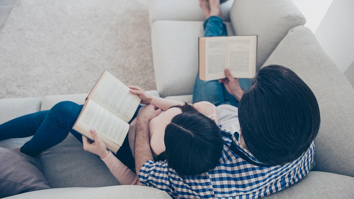 Top view portrait of well read lettered couple enjoying reading novel poem, poetry fans, lying on sofa having books in hands. Hobby free time self development education concept