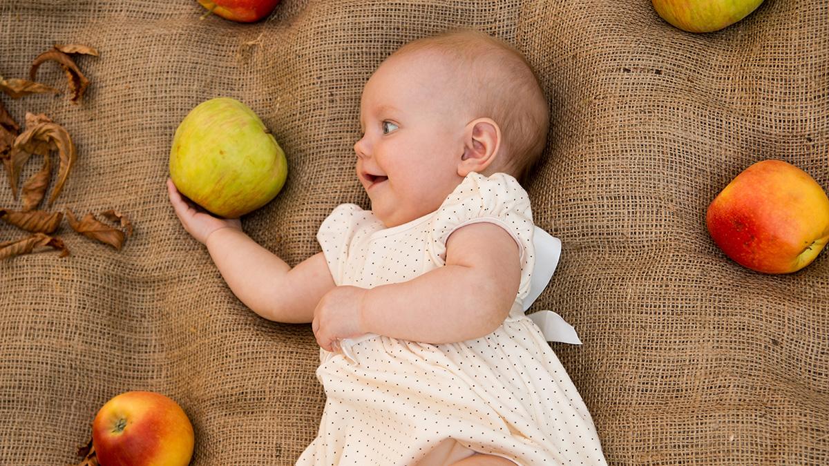 A baby holds an apple, a popular fruit to celebrate September birthdays.