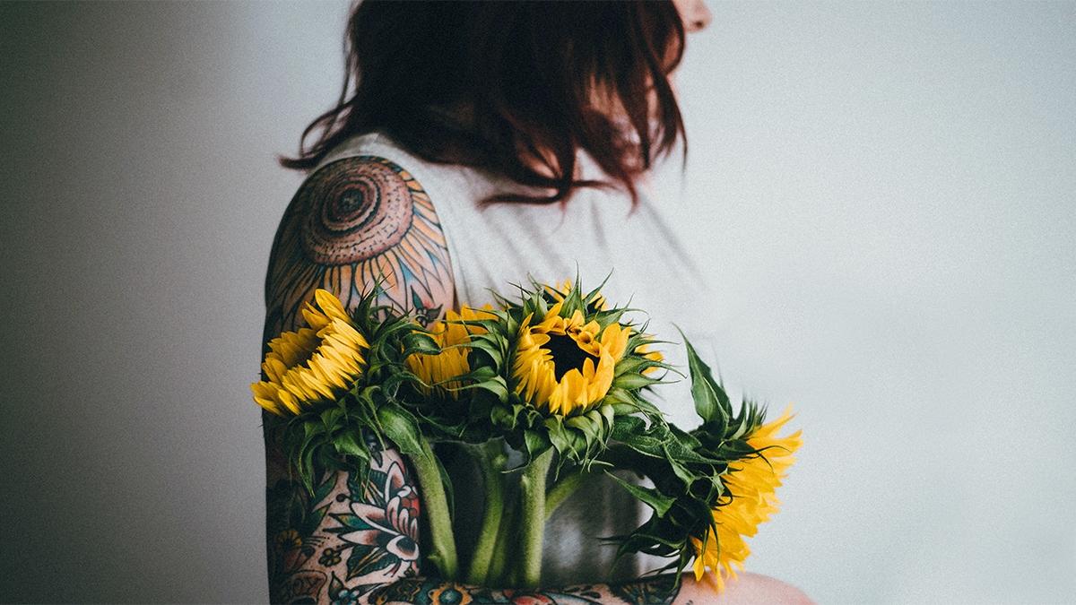 A woman holding sunflowers next to her flower tattoo
