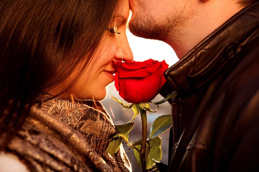 Happy and loving couple for Valentine's Day. Amorous guy gently kissing his girl in the forehead while she is enjoying the smell of the magnificent red rose. Affectionate Couple with red rose on the rooftop.
