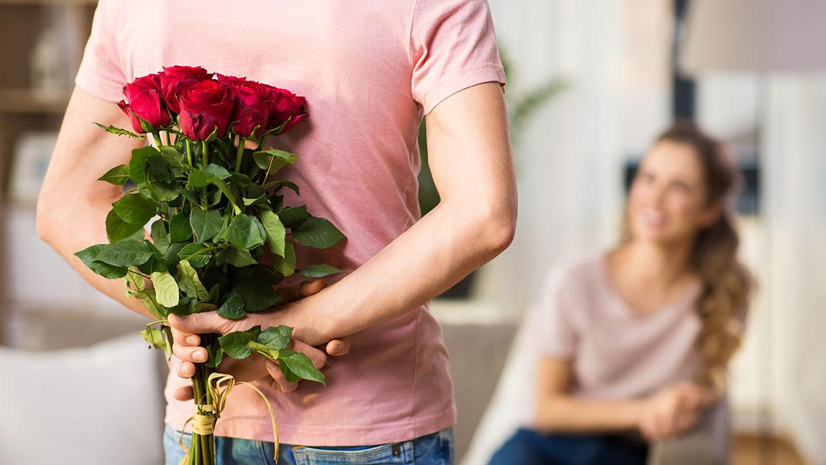 couple, relationships and people concept   happy woman looking at man hiding bunch of roses behind his back