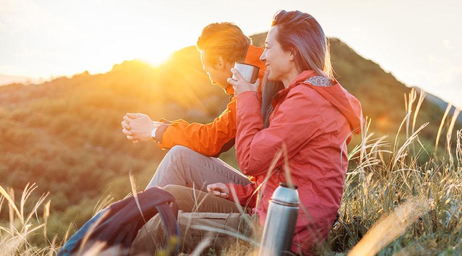 Two people outdoors on a mountain hiking sitting down drinking coffee