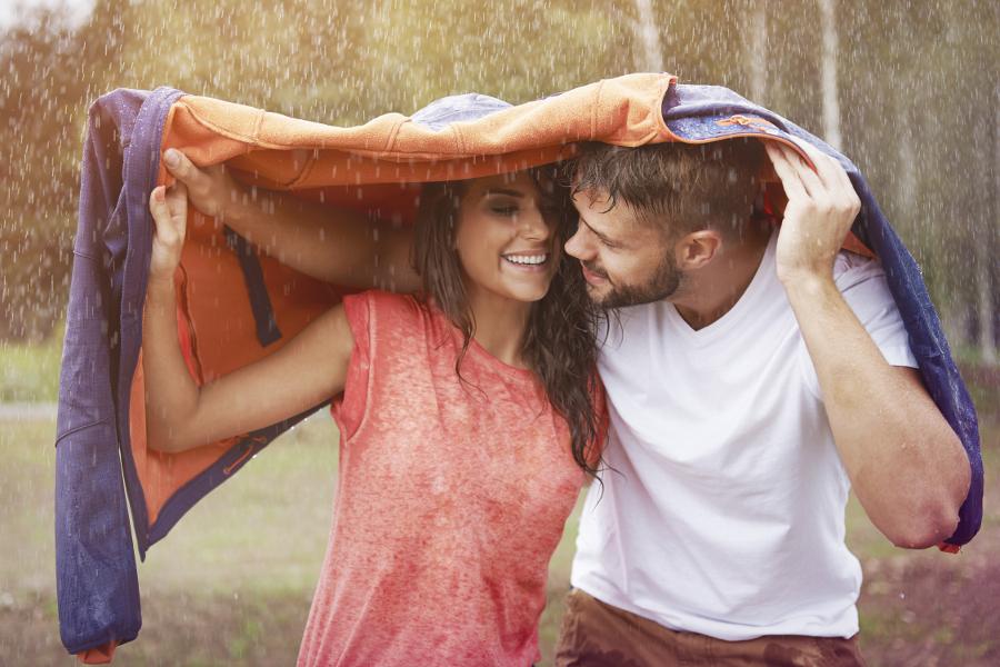 Rainy day date ideas with a couple underneath a jacket hiding from rain.