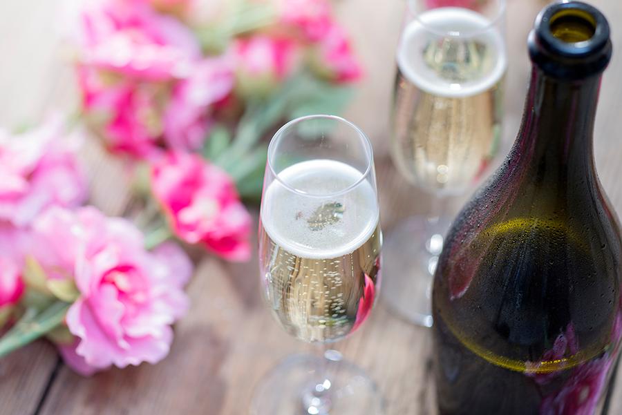 wine and flower pairings with Bottle of Prosecco and two champagne glasses on a rustic garden picnic table with flowers in the background.