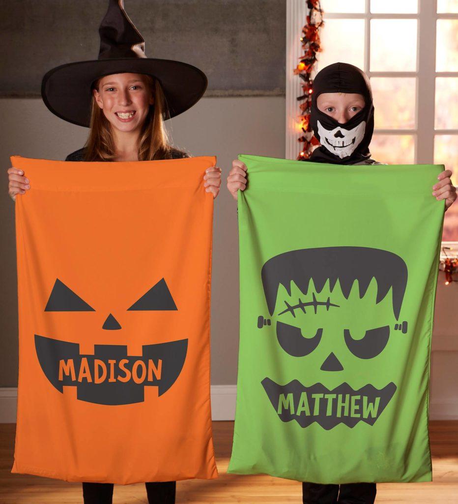 A photo of two children holding personalized spooky pillow cases, which are a great way to boost the Halloween decor of a bedroom.