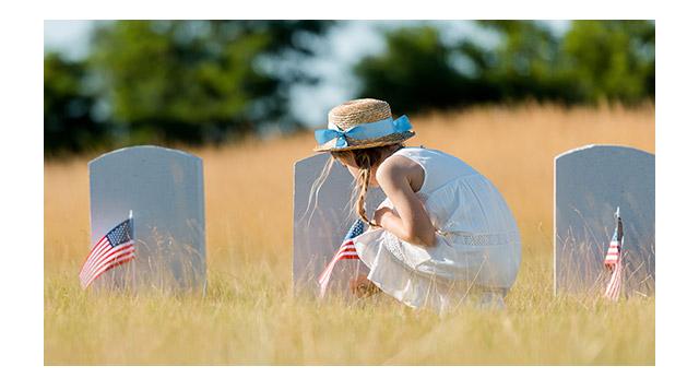 Photo of a woman decorating a grave with flag for Memorial Day