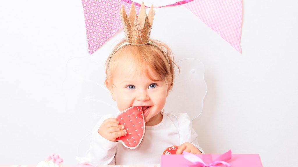 a photo of first birthday party tips with a baby eating a heart shaped cookie