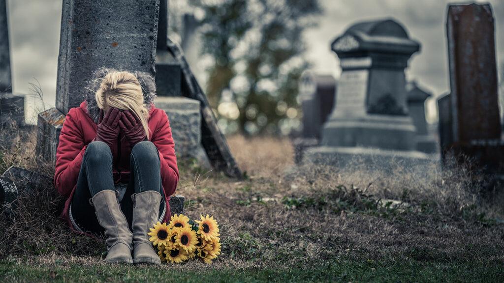 women sitting in front of grave with flowers grieving