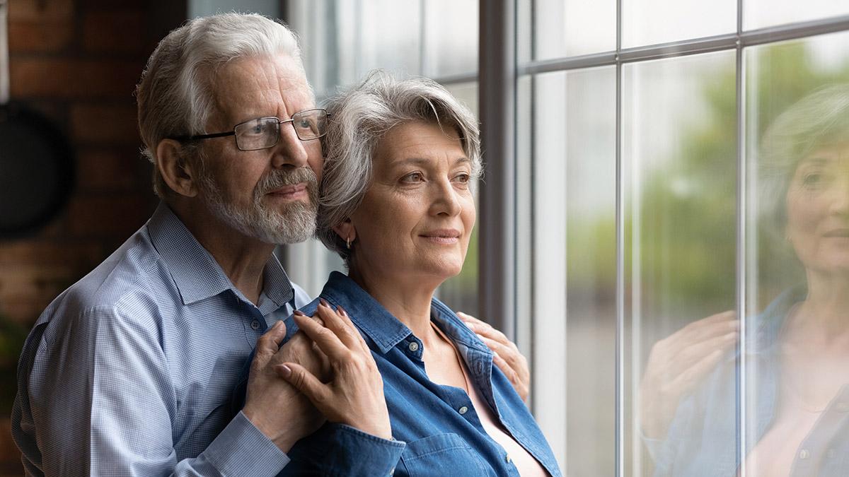 Elderly spouses hug look at window meet twilight years together
