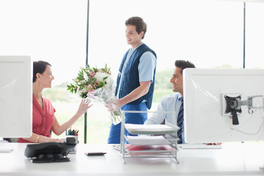 gift giving with man delivering flowers to woman in an office