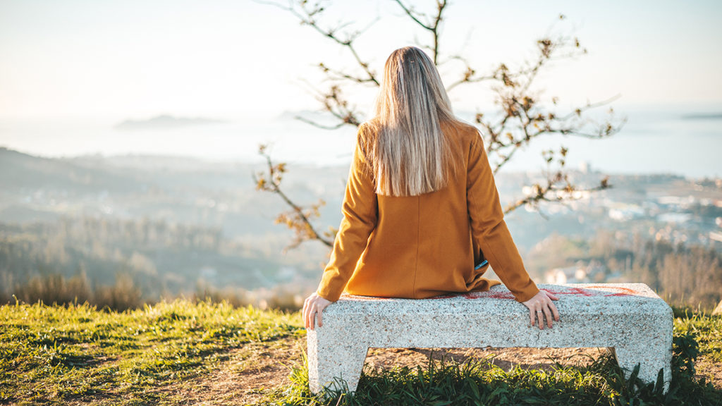 Anxiety after loss with a woman sitting on a bench outside with her back to the camera.