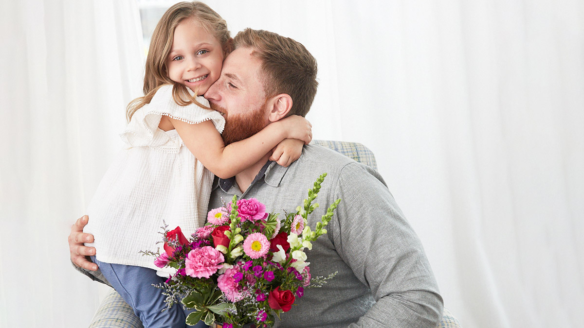 https://www.flowers.com/blog/wp content/uploads///history of mothers day with father and daughter embracing with flowers